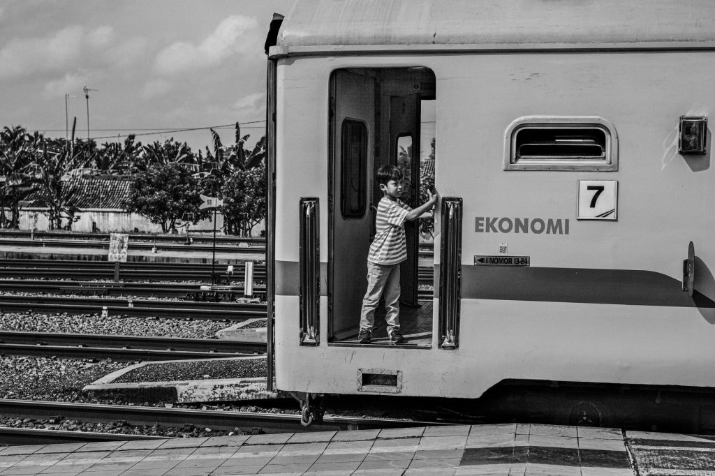 A child standing in the doorway of an Indonesian train at a Jakarta station.