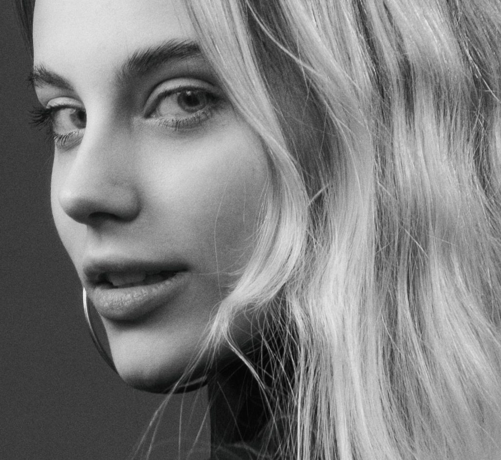 Elegant black and white close-up portrait of a woman with wavy blonde hair and smooth skin.