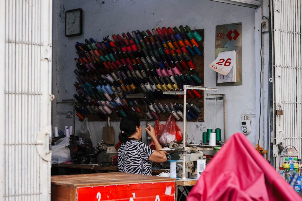 A tailor working at a sewing machine in a shop filled with colorful spools of thread.
